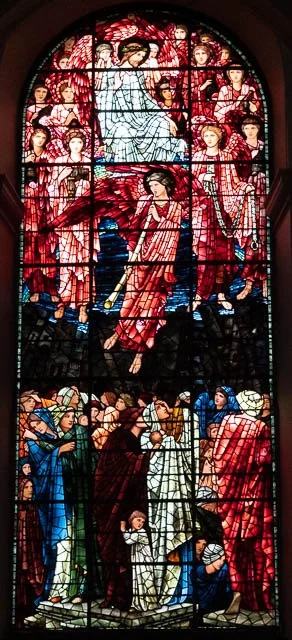 Stained glass window depicting a religious scene with a woman surrounded by angels at the top and various figures below, some kneeling or praying.