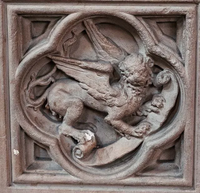 Carved stone relief of a dragon with wings and claws, set in a square frame.