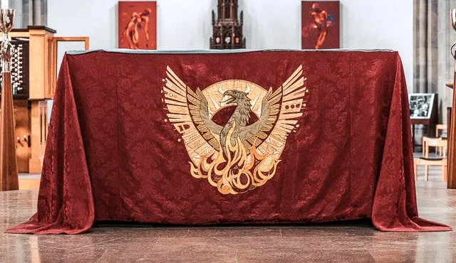 A red cloth with a gold eagle emblem is draped over a table in a room with artwork and wooden furniture.