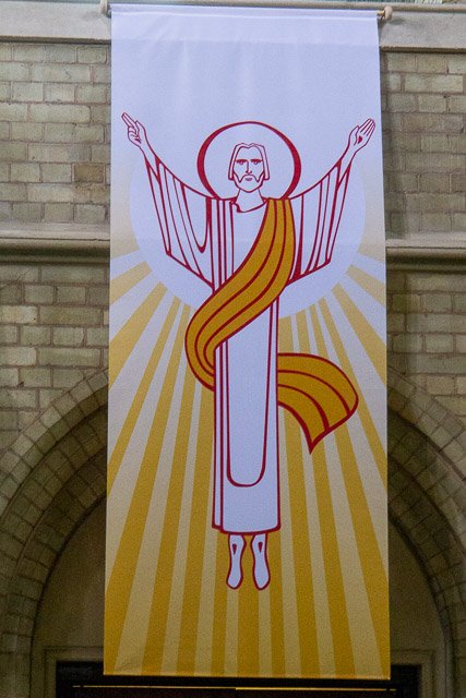 Drawing of Jesus Christ with outstretched arms, a halo, and long hair, with radiant yellow lines in the background.