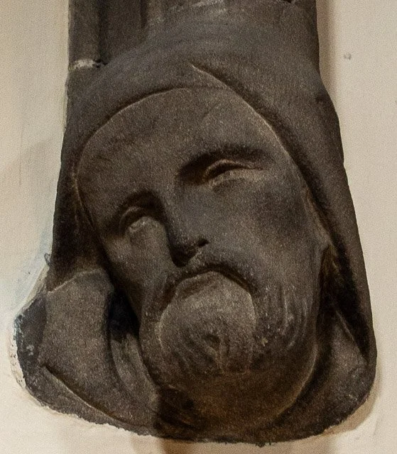 Close-up of a carved stone sculpture depicting a face with a beard and head covering.