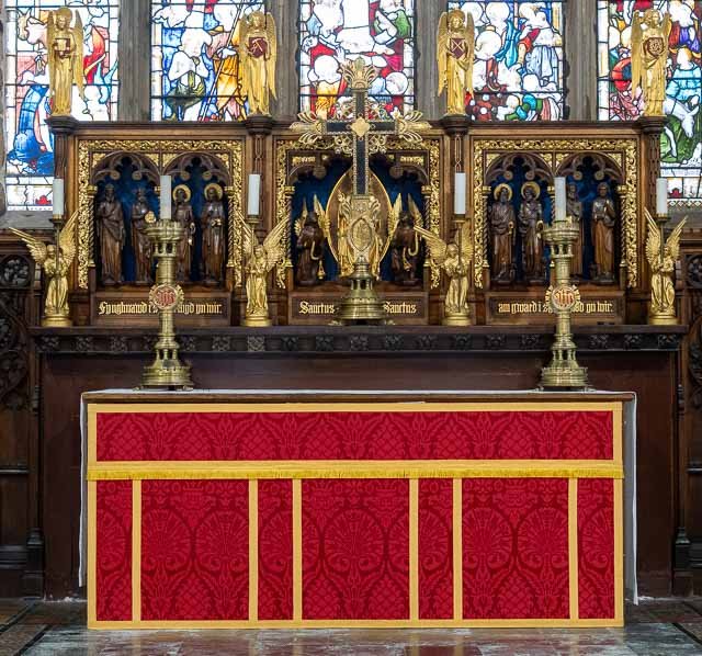 Religious altar with gold statues of saints and angels, featuring a large central crucifix, set behind stained glass windows in a church.