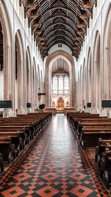 Interior of a large church with high vaulted ceiling, wooden pews, and stained glass windows at the altar