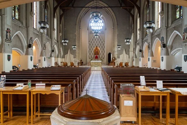 Inside of a church with wooden pews, an altar at the front, and stained glass windows.