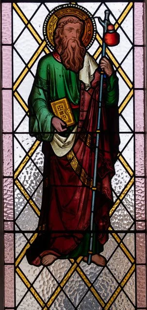 Stained glass window depicting a bearded man with a halo, holding a book and a scepter, dressed in green and red robes.