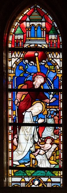 Stained glass window depicting a biblical scene with a woman, a man, a dog, and architectural elements.