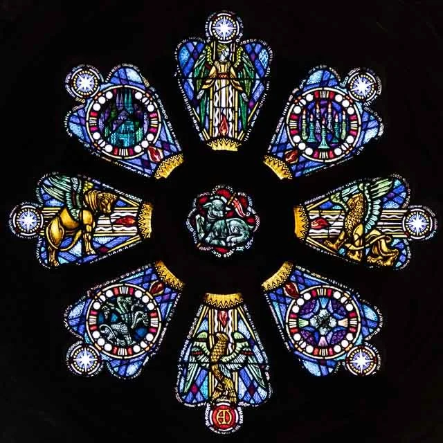 Colorful stained glass window with religious figures and symbols arranged in a circular pattern.