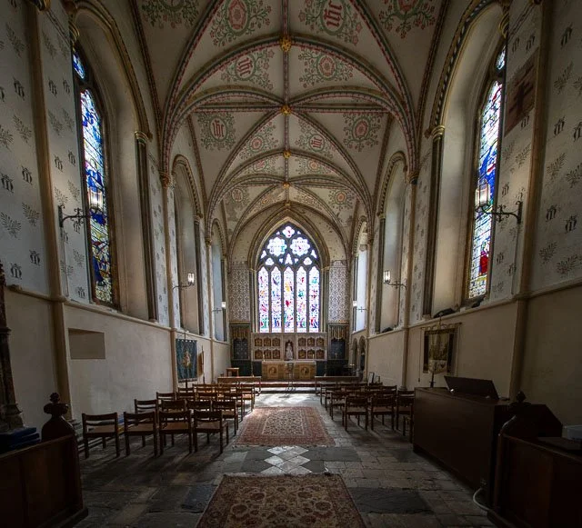 Interior of a historic church with stained glass windows, wooden pews, and ornate vaulted ceilings.
