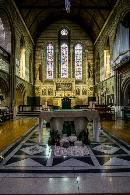Inside a church with stained glass windows, an altar with a white cloth, candles, and religious decorations.