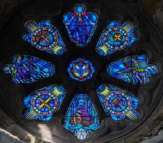 Colorful stained glass window with biblical scenes and symbols in a circular pattern.