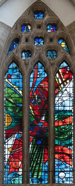 Colorful stained glass window depicting a red dragon with green wings and a blue background, surrounded by decorative stone framing.