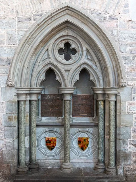 Stone gothic architecture with arched windows, columns, and plaques, possibly a historical or memorial monument.