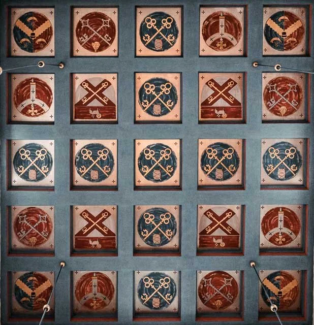 A set of 25 chess-like tiles arranged in a 5x5 grid. The tiles feature patterns of crossed keys, circular designs, and lines, with some resembling compasses or swords, in alternating color schemes of blue, red, and tan.