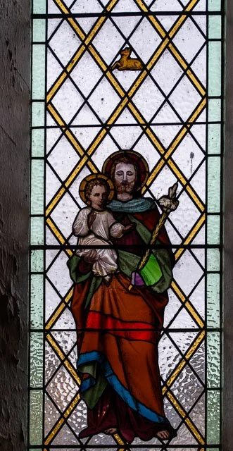 Stained glass window depicting Jesus Christ holding a young child, with a halo and a dove above.