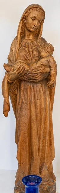 Wooden sculpture of a woman holding a baby, set against a plain background.