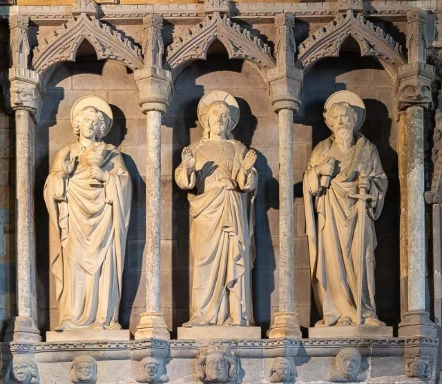 Three stone religious statues of saints on a church wall with Gothic arches and columns.