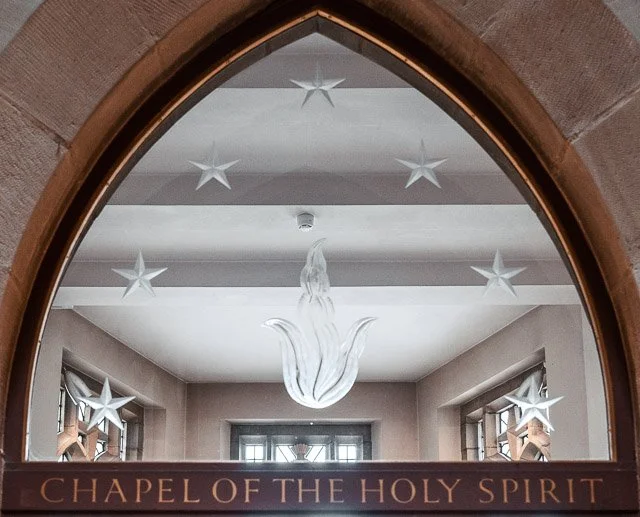 Interior view of the Chapel of the Holy Spirit with star-shaped decorations hanging from the ceiling and a large glass chandelier in the center.
