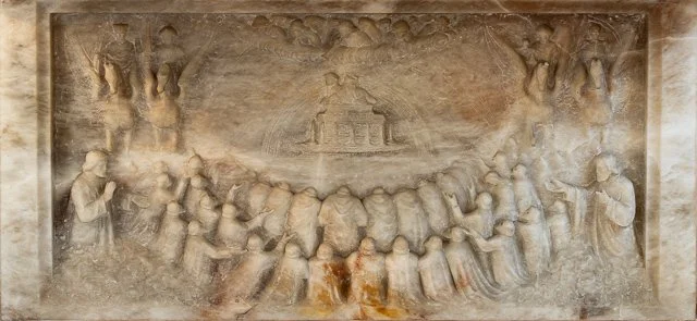 Stone relief carving depicting a historical scene with multiple figures, some playing musical instruments, and others gathered in a ceremonial setting.