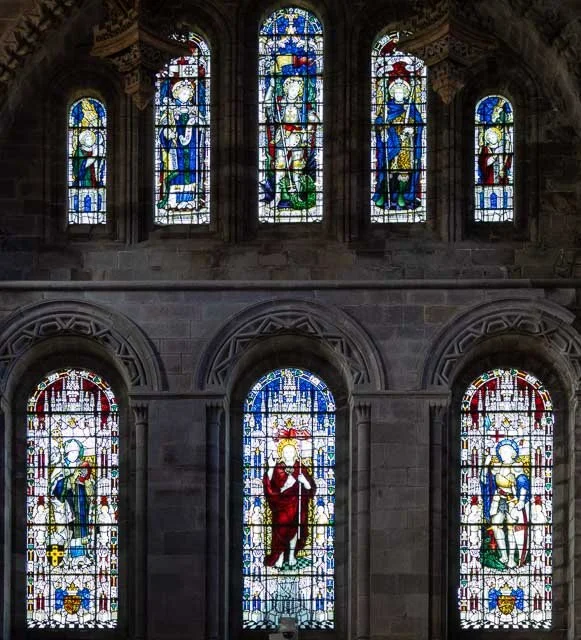 Colorful stained glass windows in a church, depicting various religious figures and scenes, with intricate designs and vibrant colors.