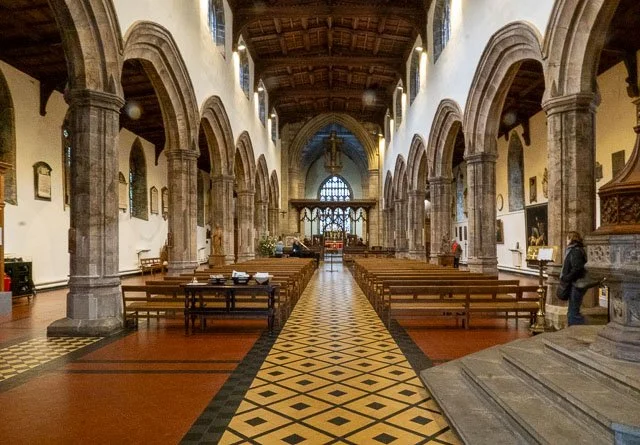 Interior of a historic church with high vaulted ceilings, stone columns, wooden pews, and religious artwork.