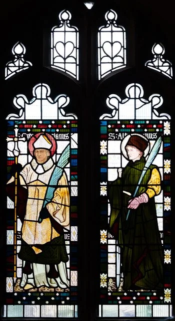 Stained glass window depicting two saints or biblical figures holding swords, with decorative church architecture in the background.