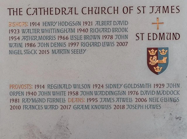 A memorial wall listing the names of bishops and provosts of St. James Cathedral, with their years of service, along with the cathedral's coat of arms.