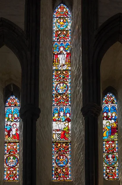 Colorful stained glass windows in a church depicting religious scenes and figures.