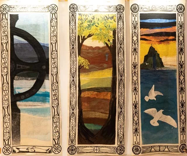 Triptych painting with left panel of a ship's steering wheel and a blue sky with ocean waves, middle panel of a large tree with green and yellow leaves overlooking a landscape, and right panel of a sunset over the ocean with seagulls in flight and a 