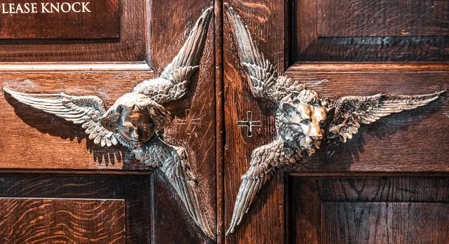 Decorative door with two winged animal sculptures and a 'Please Knock' sign.