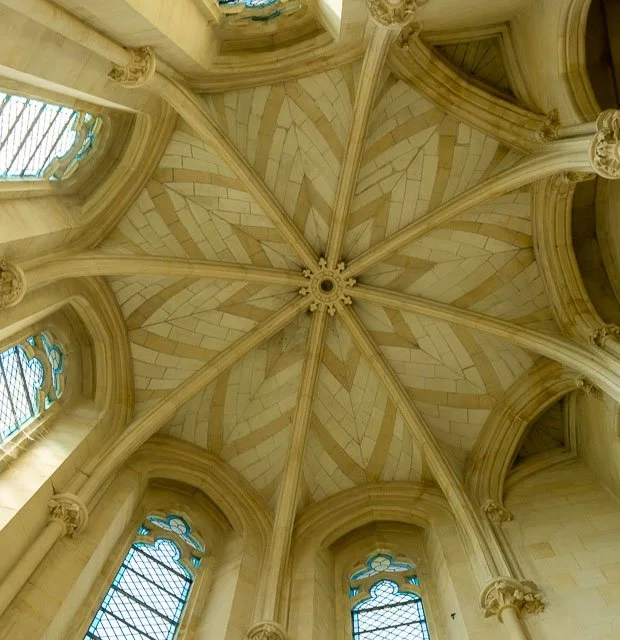 Ceiling of a gothic cathedral with ribbed vaults and stained glass windows.