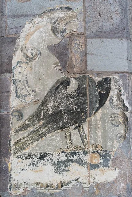Ancient stone carving of a bird, possibly a raven, with decorative elements around its head, on a brick wall