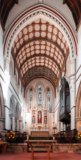 Interior of a historic church with vaulted ceiling, ornate wooden accents, stained glass windows, and an altar at the front.