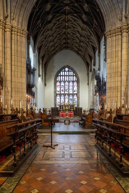 Interior view of a historic church with stained glass windows, wooden pews, and a high vaulted ceiling.