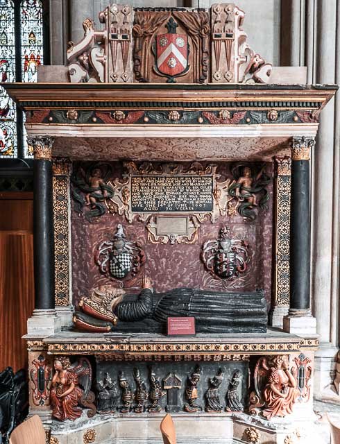 Ornate historical monument with carved figures, coats of arms, and Latin inscriptions inside a church or cathedral.
