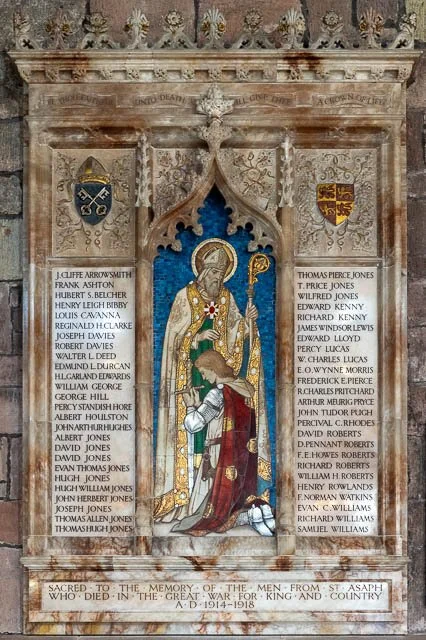A stained glass window depicting Saint King David with a crown and scepter, surrounded by an ornate wooden frame, flanked by gray stone walls with inscriptions and coats of arms, and a commemorative plaque at the bottom.