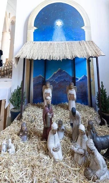 Nativity scene with figurines of Mary, Joseph, baby Jesus, the Wise Men, shepherds, and animals in a straw setting, with a backdrop of mountains and a starry night sky featuring the Star of Bethlehem.