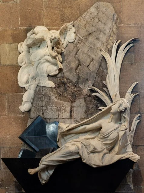Sculpture of a reclining woman with flowing hair and draped clothing, surrounded by ornate clouds and decorative elements.