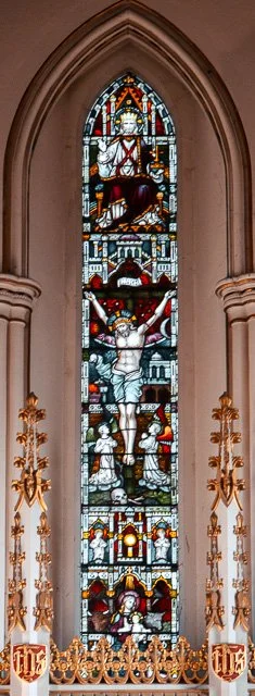 Stained glass window depicting a religious scene with a central figure on a cross, surrounded by other figures, set in a church.