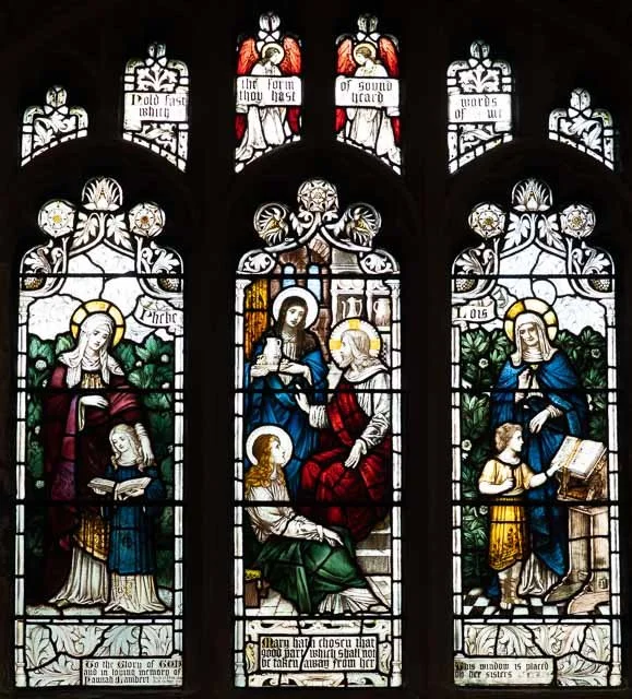 Stained glass window depicting religious scenes with Mary, Jesus, and children, with biblical inscriptions.