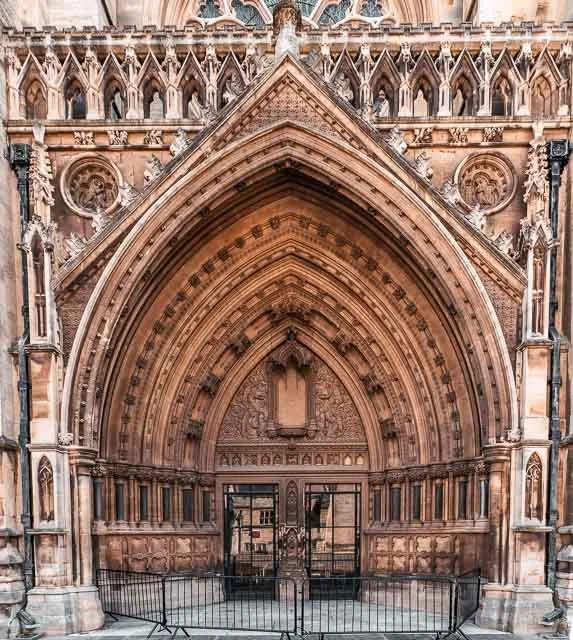 Close-up view of an ornate medieval-style cathedral entrance with pointed arches, detailed carvings, and a metal gate.