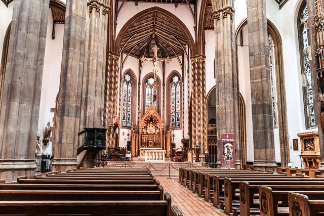 Interior of a historic church with wooden pews, stained glass windows, and ornate altar.