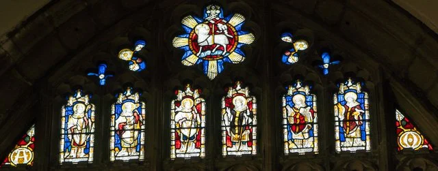 Colorful stained glass windows in a church with religious figures and symbols.