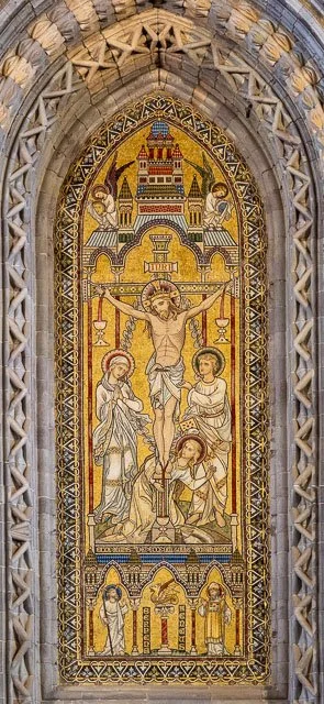 A religious mosaic depicting Jesus Christ on the cross, surrounded by saints and angels, with a cityscape in the background, framed by an ornate Gothic arch.