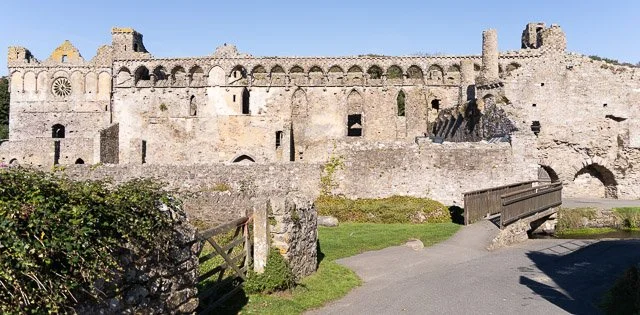 Ruins of an old stone castle or fortress with archways and towers, surrounded by grass and a dirt path