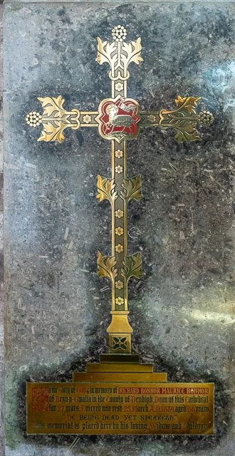 A decorative cross monument with gold accents on a stone surface, featuring an inscription at its base.