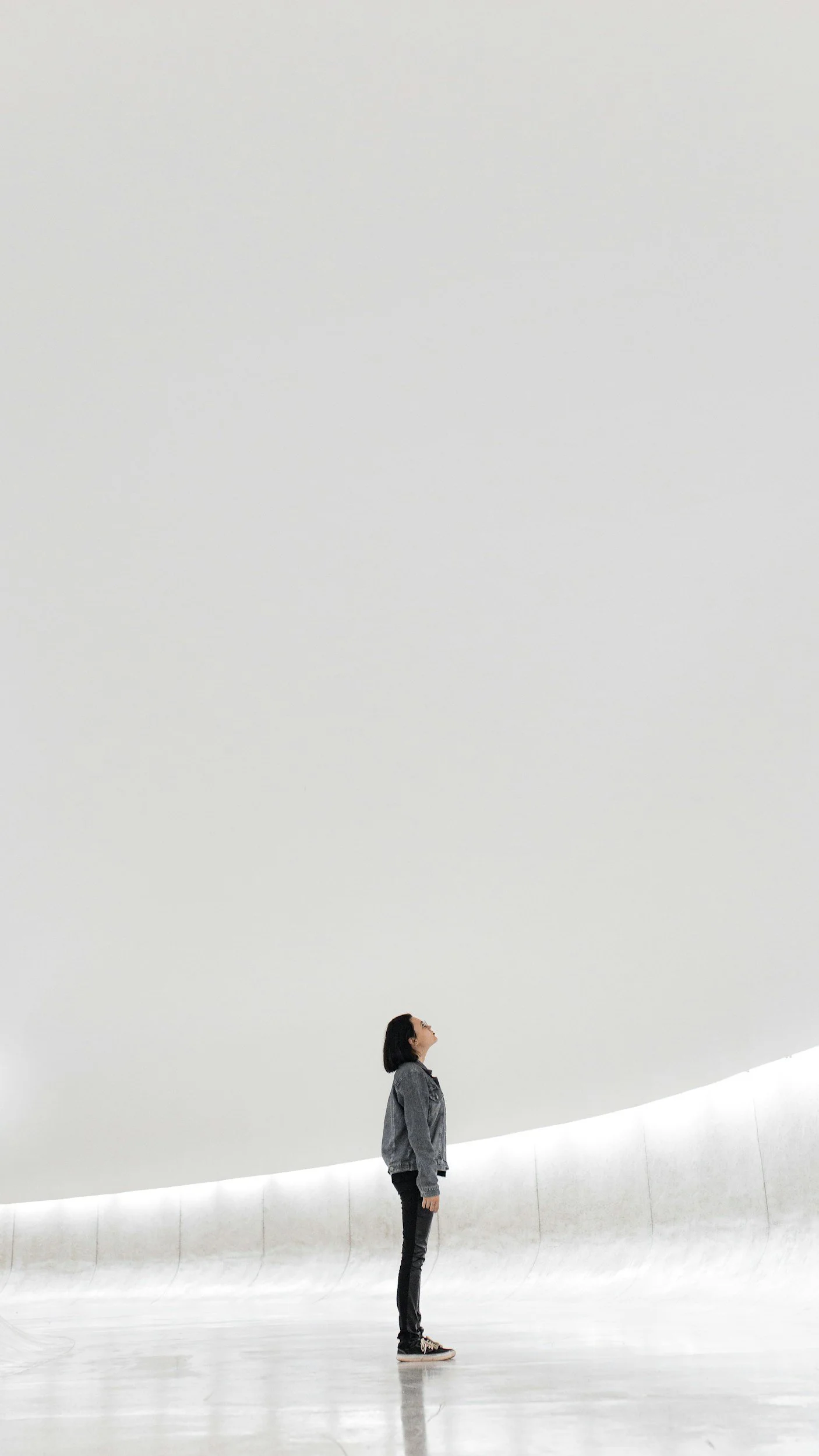 Eine junge Frau steht in einem großen, weißen, minimalistischen Raum und blickt nach oben.