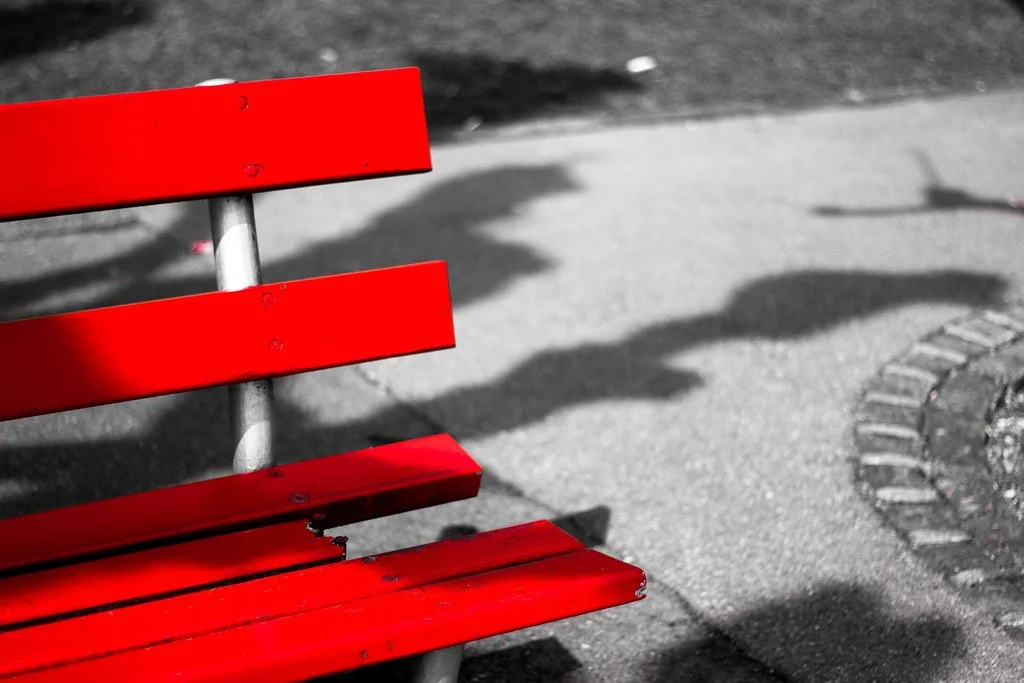 Roter Parkbank mit Schatten auf Gehweg