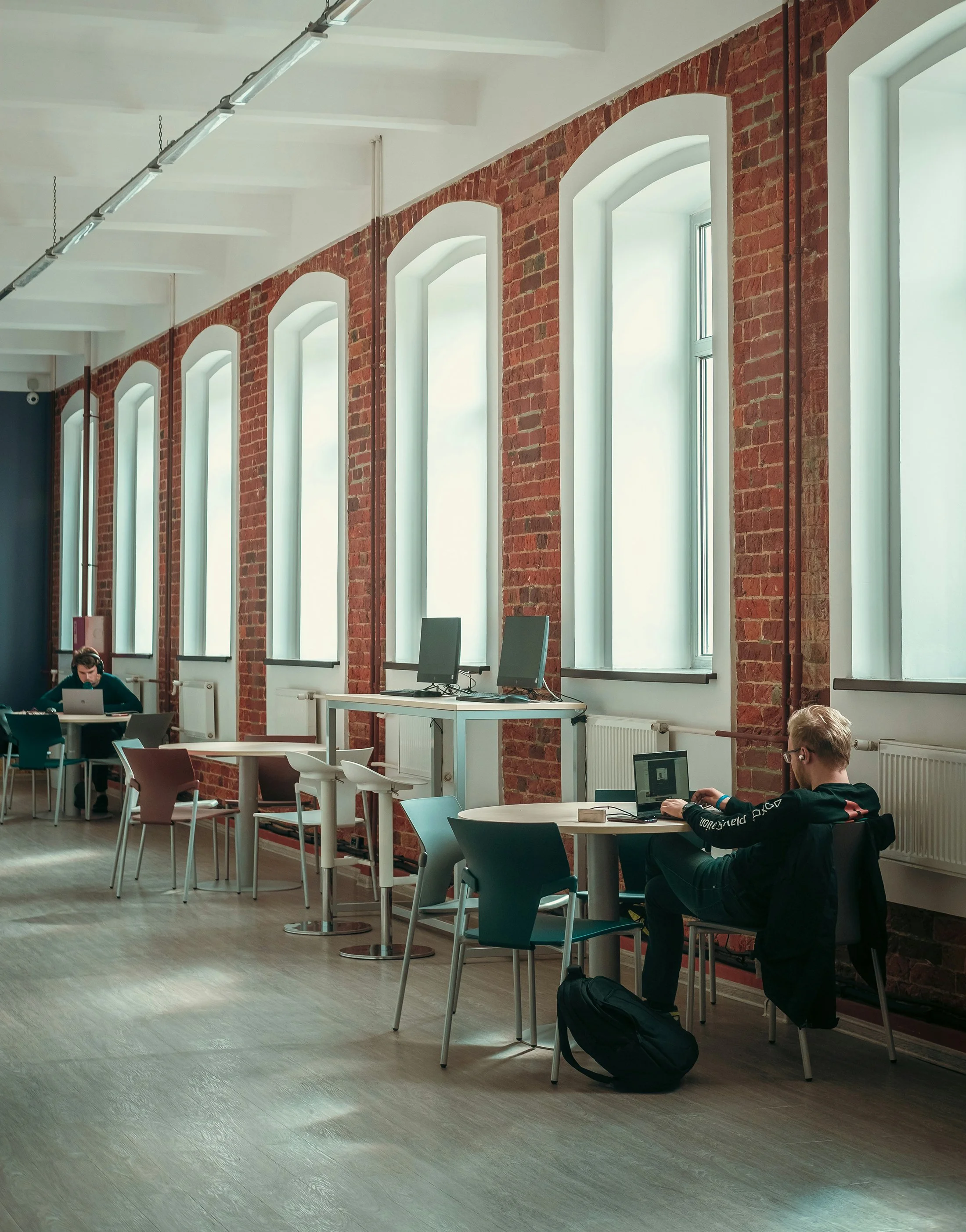 Ein moderner Lernraum mit großen Fenstern, roten Ziegelwänden und Schüler, die an Laptops arbeiten.