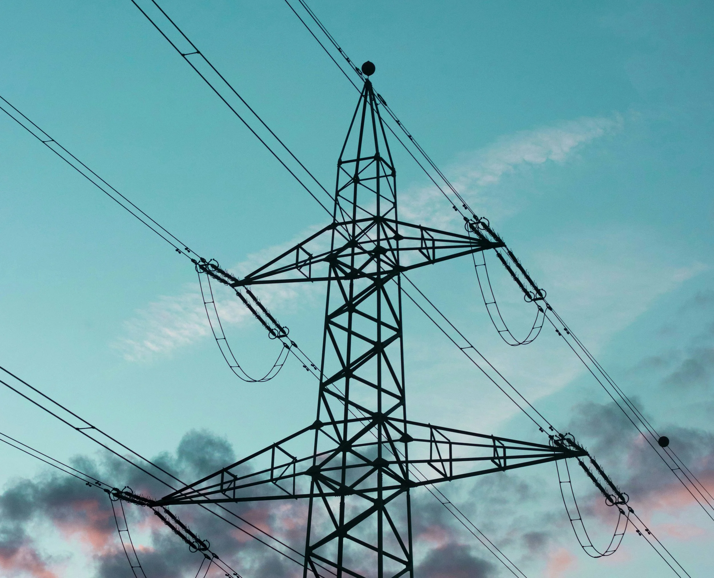 Strommast mit Kabeln vor einem bewölkten Himmel bei Dämmerung.