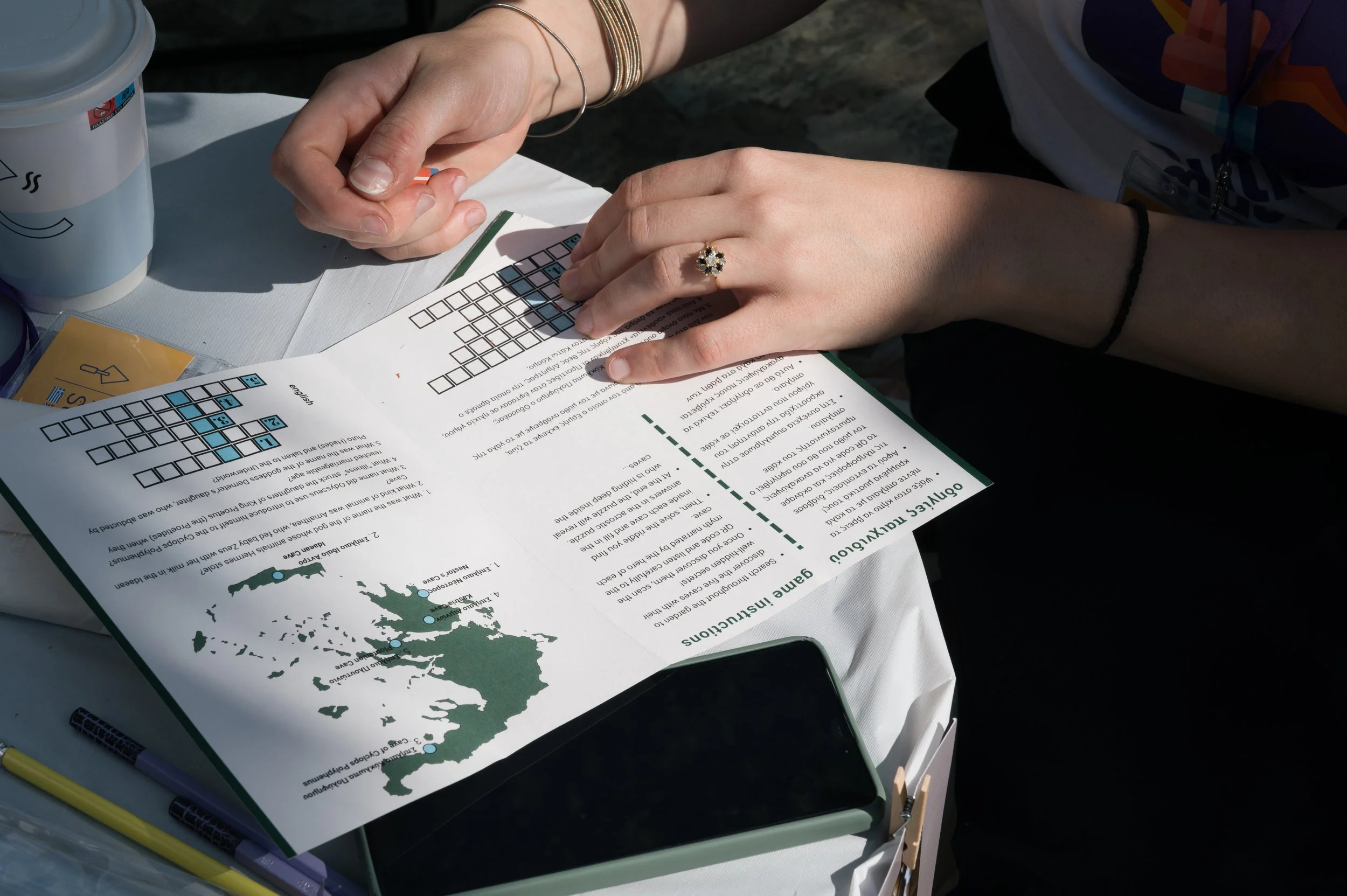 A person filling out a map quiz at a table, with a map of Greece and instructions on the paper, surrounded by pens and a cup.